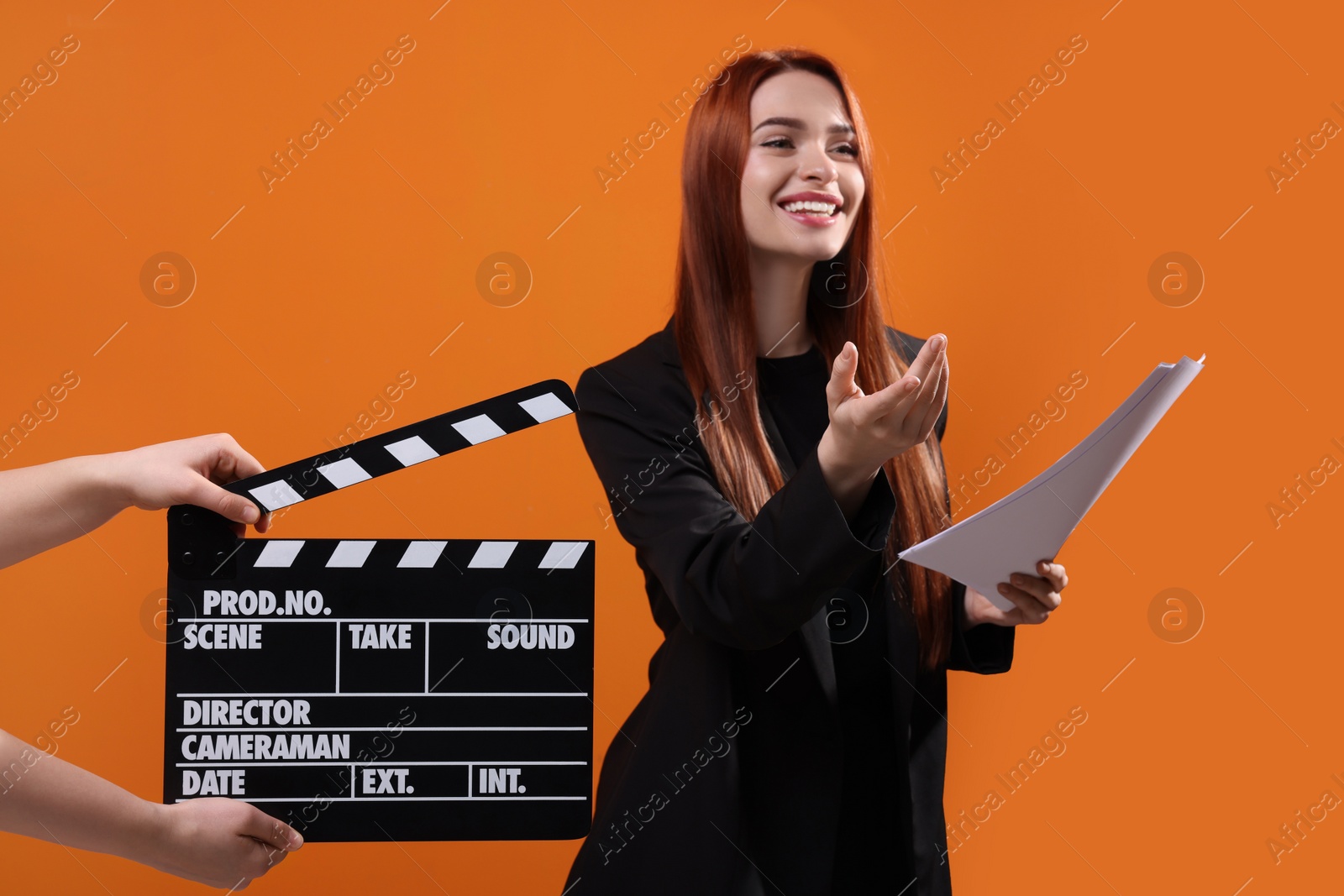 Photo of Actress performing role while second assistant camera holding clapperboard on orange background, selective focus