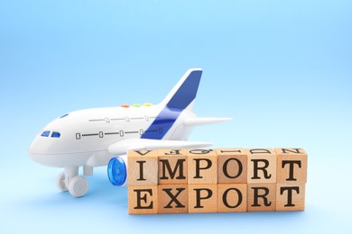 Photo of Words Import and Export made of wooden cubes, toy airplane on light blue background