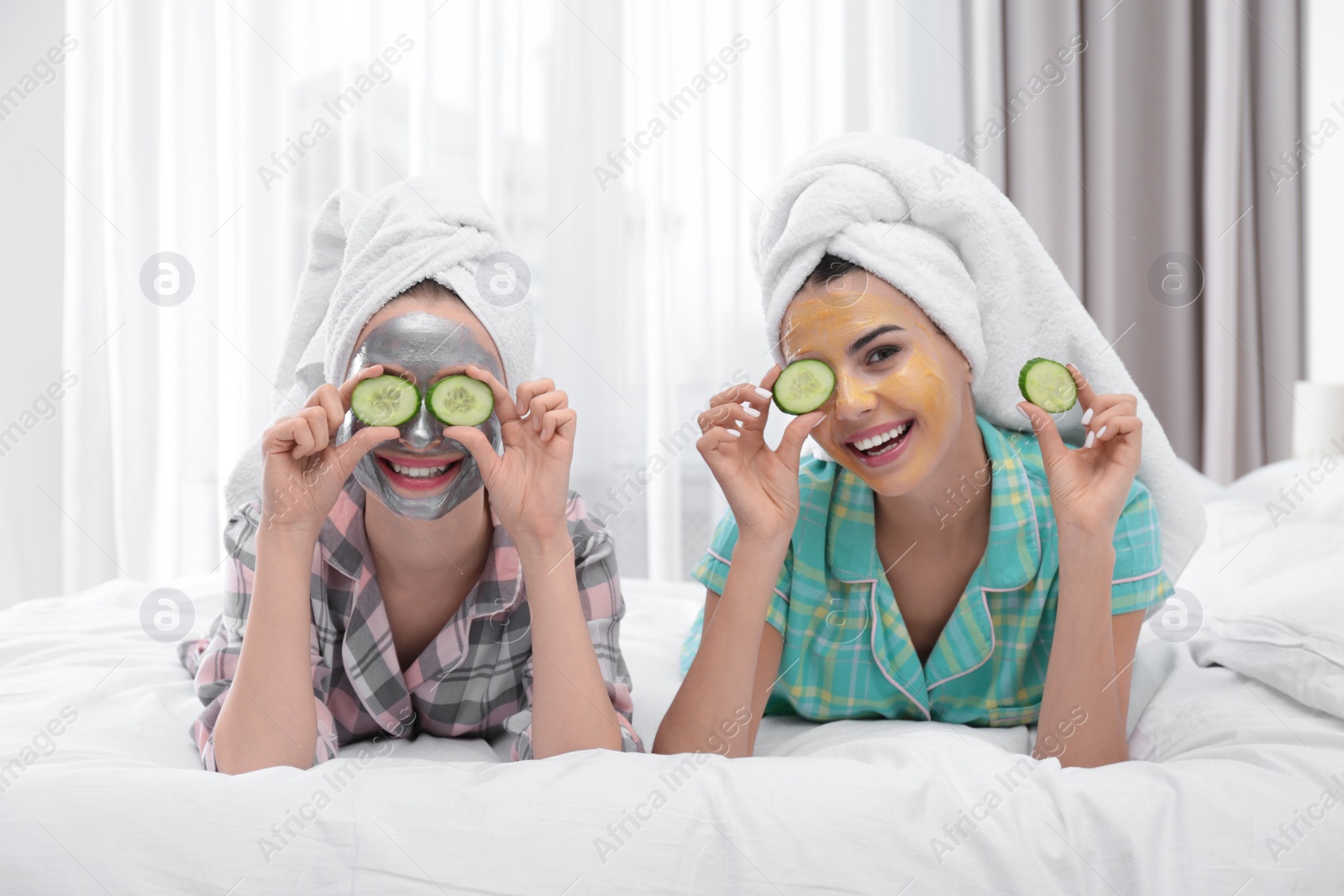 Photo of Young friends with facial masks having fun in bedroom at pamper party