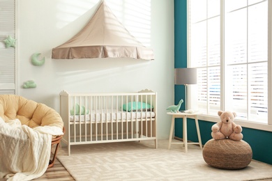 Photo of Cute nursery interior with comfortable crib near white wall