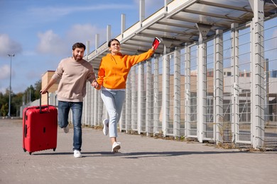 Being late. Couple with red suitcase running outdoors, space for text