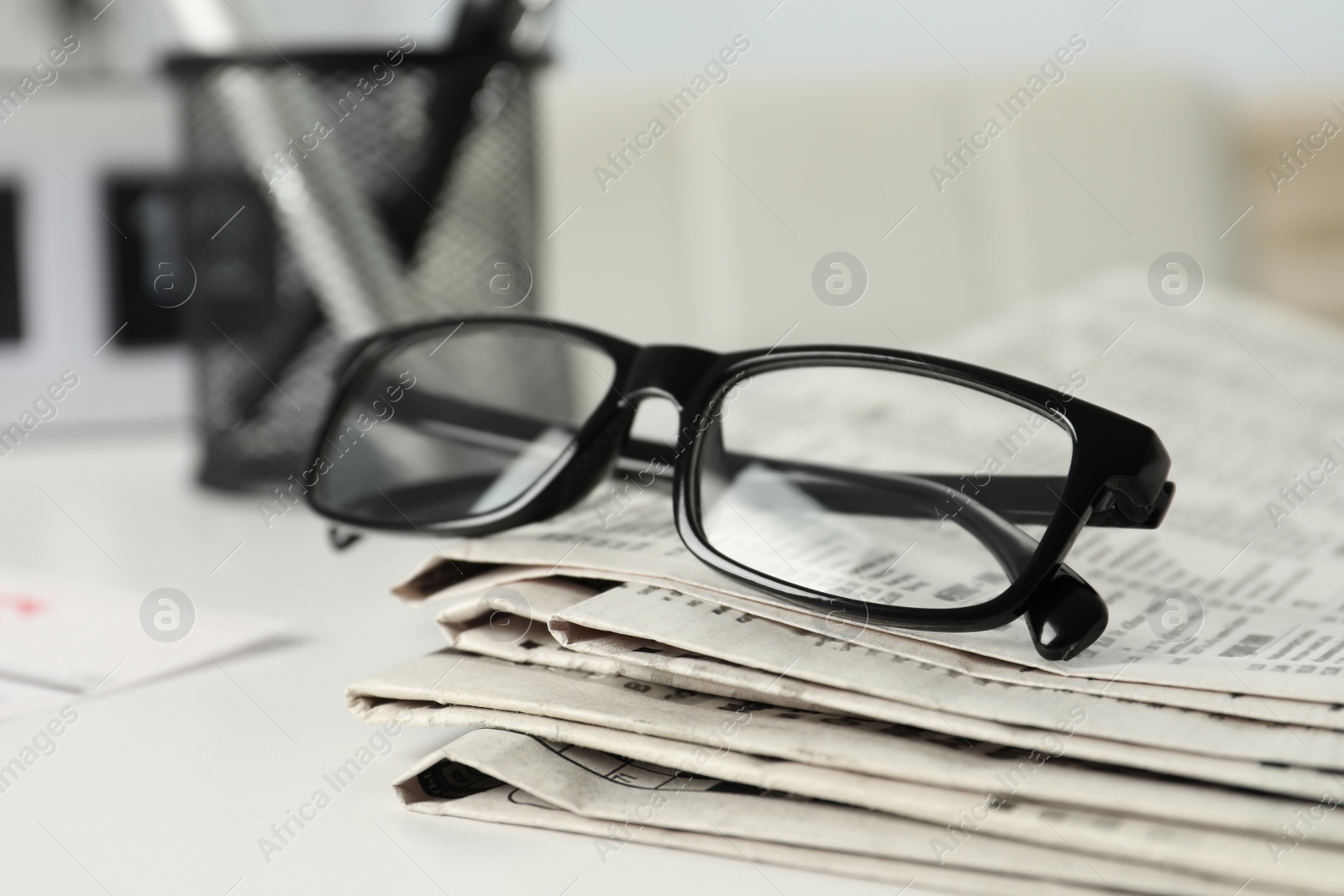 Photo of Stack of newspapers and glasses on white table indoors