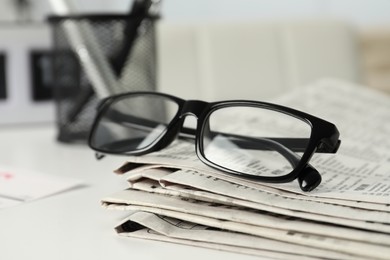Photo of Stack of newspapers and glasses on white table indoors