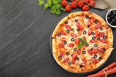 Tasty pizza with dry smoked sausages, olives, tomatoes, pepper and parsley on grey table, top view. Space for text