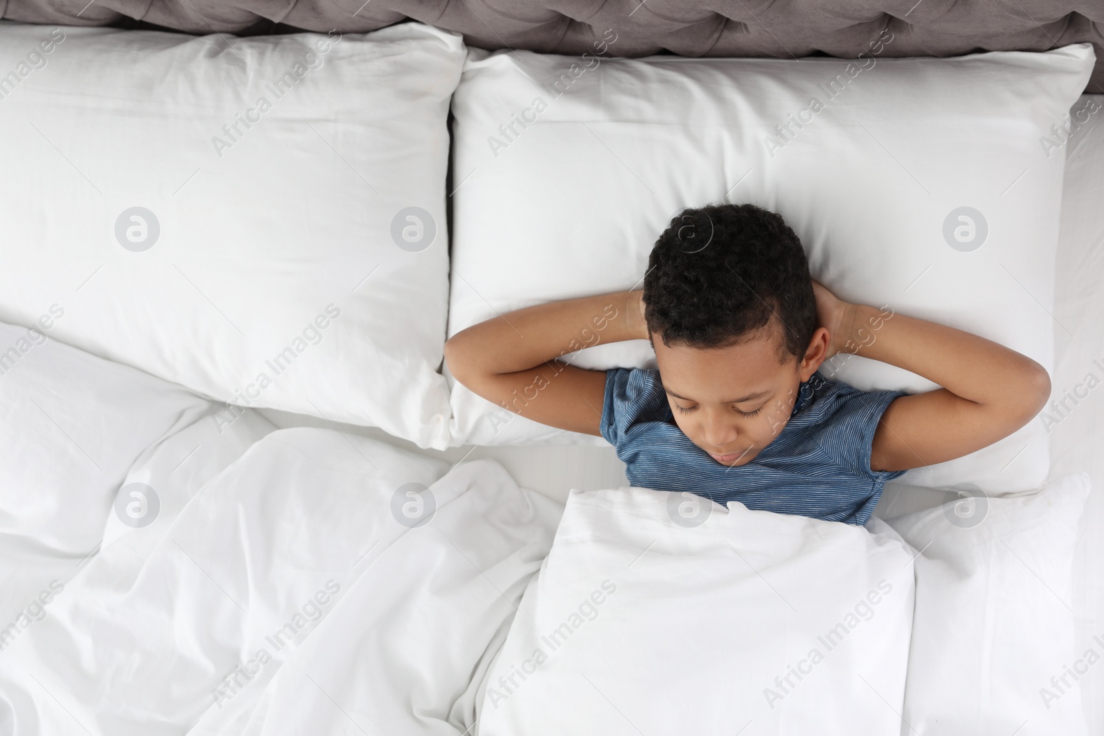 Photo of Cute little African-American boy sleeping in bed, above view