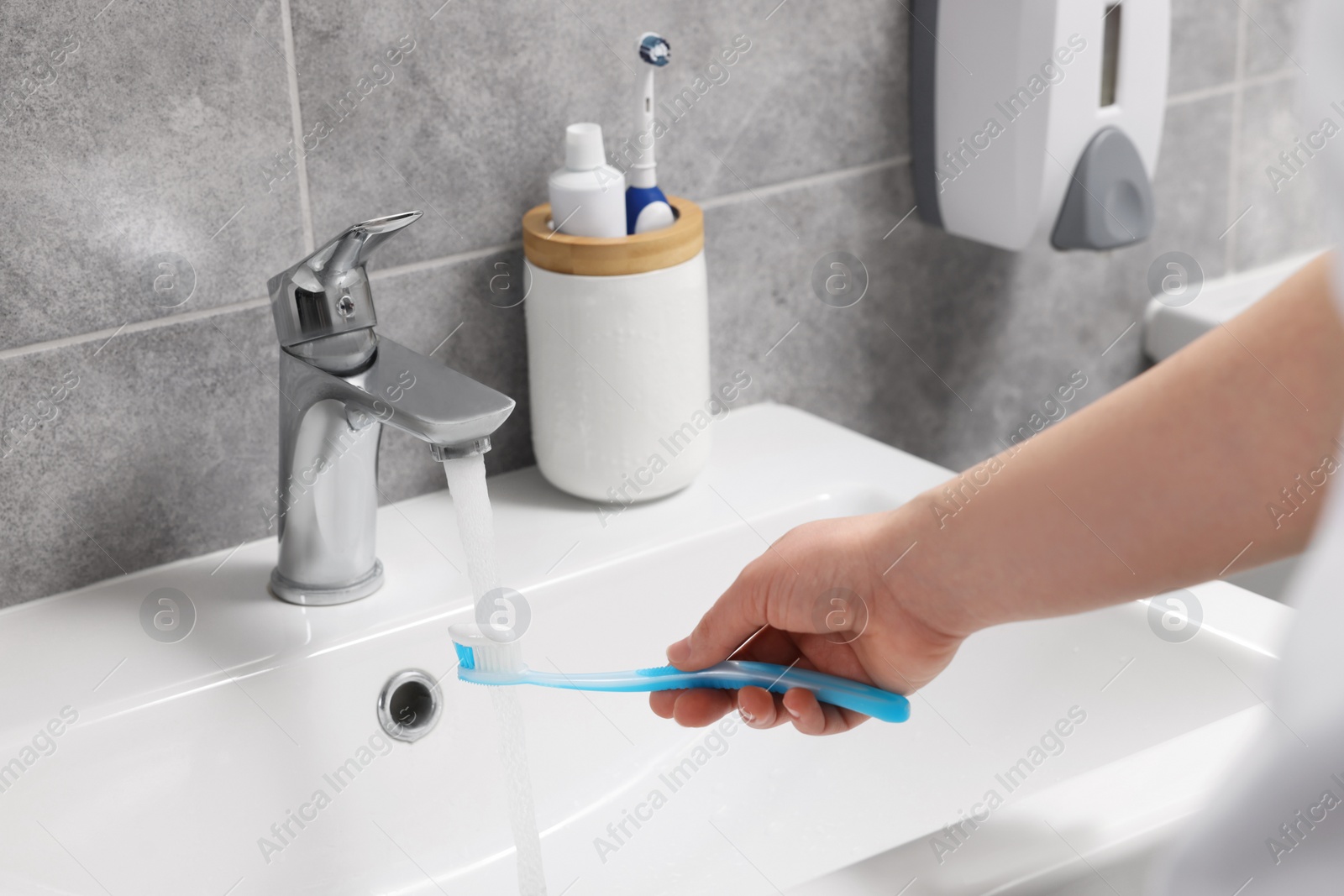 Photo of Woman washing plastic toothbrush under flowing water from faucet in bathroom, closeup