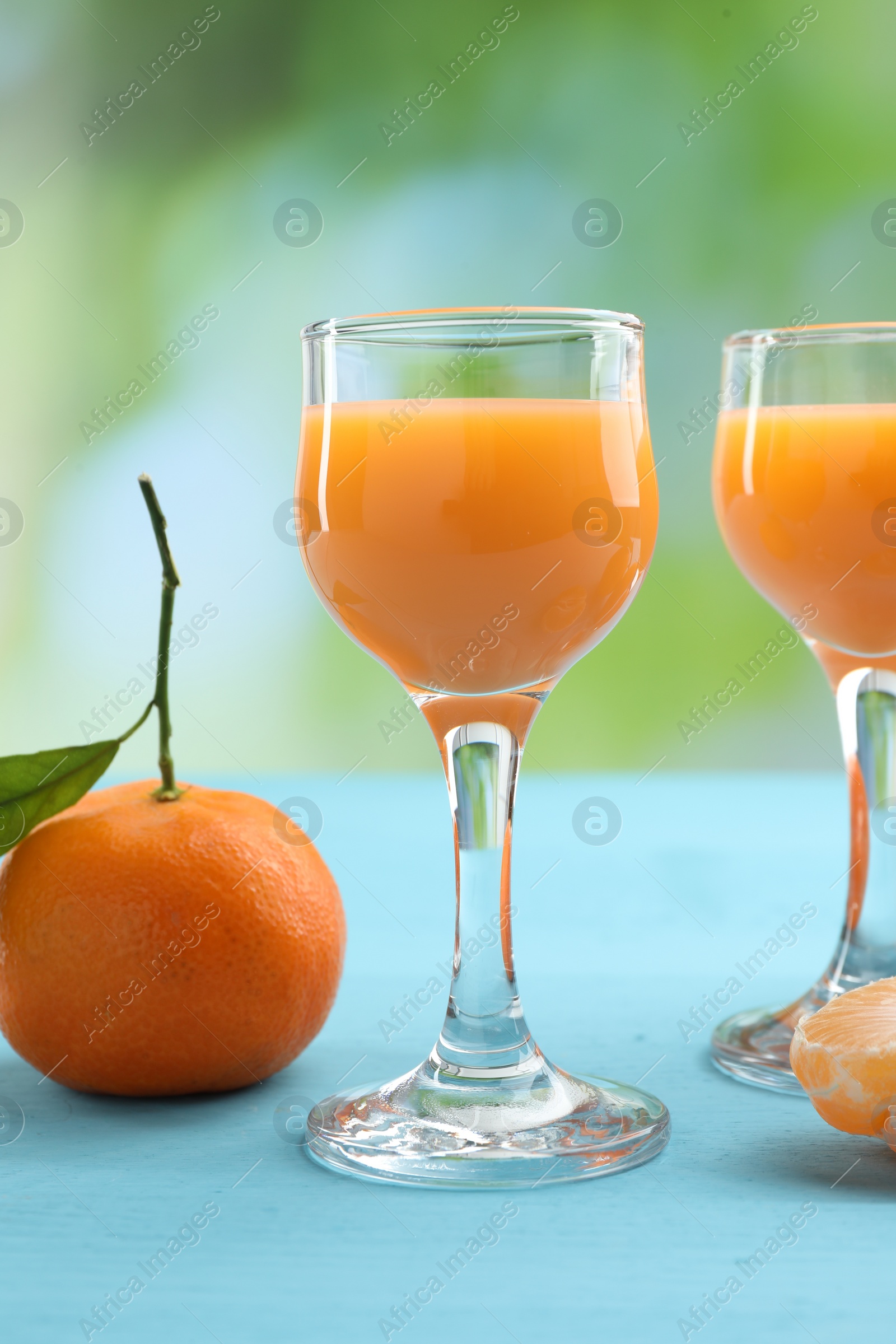 Photo of Delicious tangerine liqueur and fresh fruit on light blue wooden table