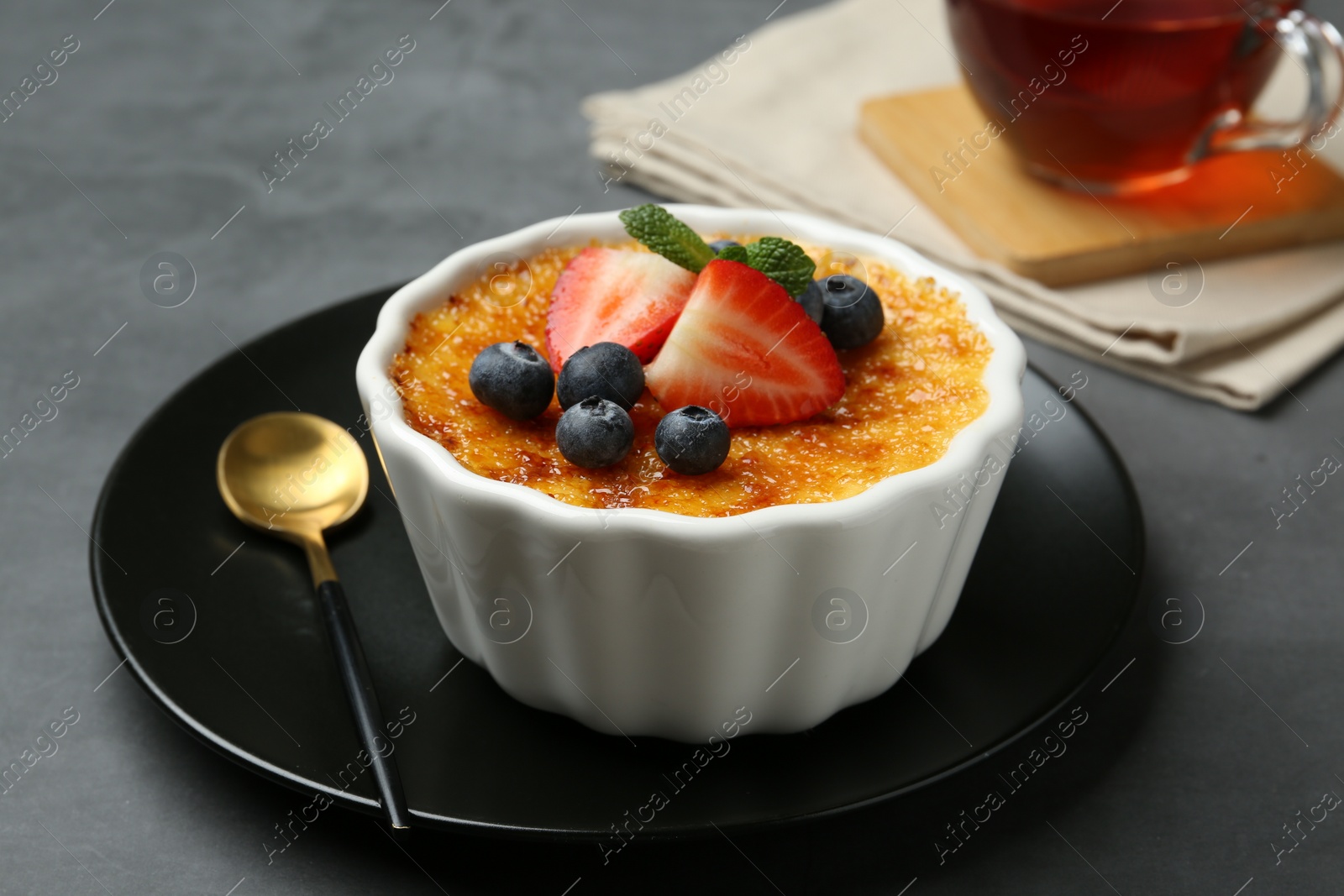 Photo of Delicious creme brulee with berries and mint in bowl on grey table, closeup