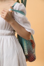 Woman with string bag of fresh vegetables on beige background, closeup