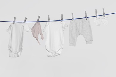 Photo of Different baby clothes drying on laundry line against light background