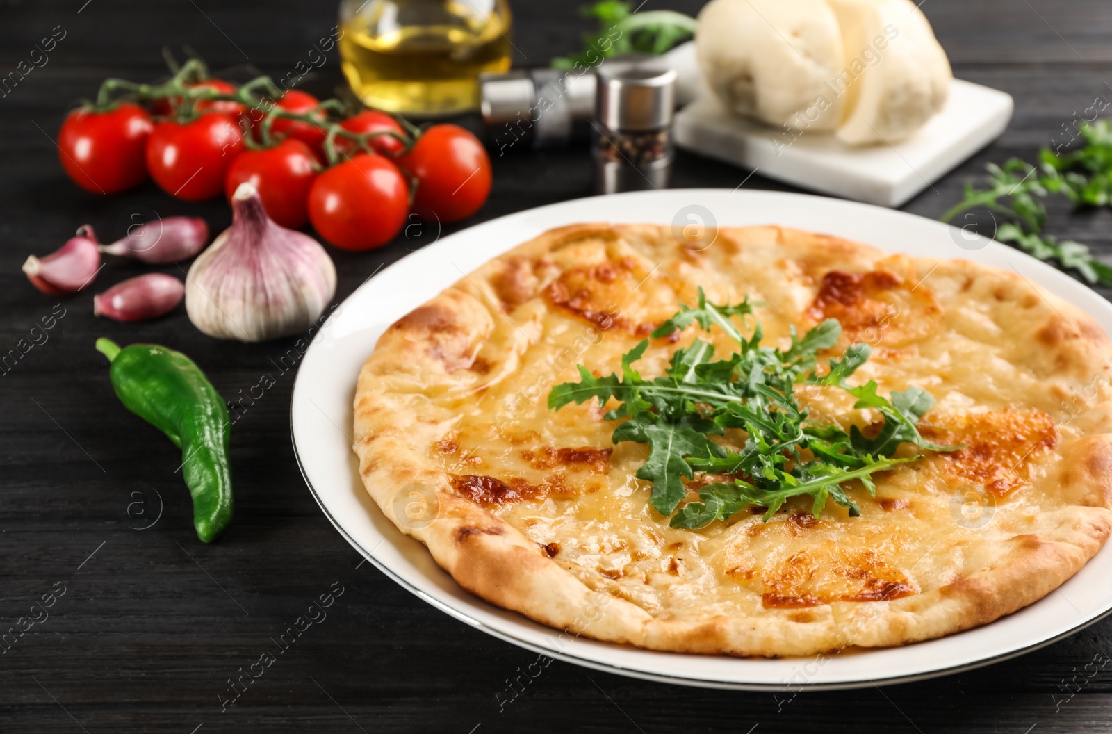 Photo of Delicious khachapuri with cheese, arugula and vegetables on dark wooden table, closeup