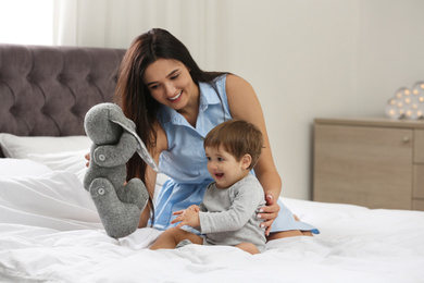 Young nanny and cute little baby playing with toy in bedroom