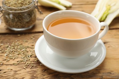 Photo of Fennel tea in cup, seeds and fresh vegetable on wooden table, closeup