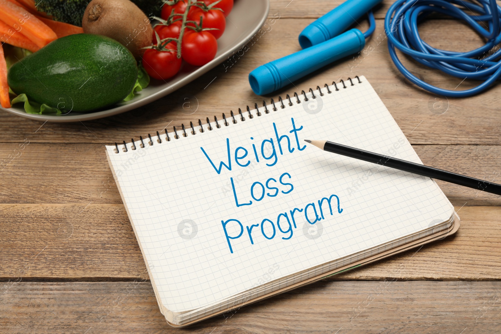 Photo of Weight loss concept. Notebook, skipping rope and different products on wooden table