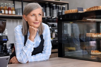 Photo of Portrait of smiling business owner at cashier desk in her cafe