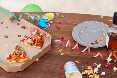 Photo of Messy table with pizza leftovers, alcohol and streamers indoors. After party chaos