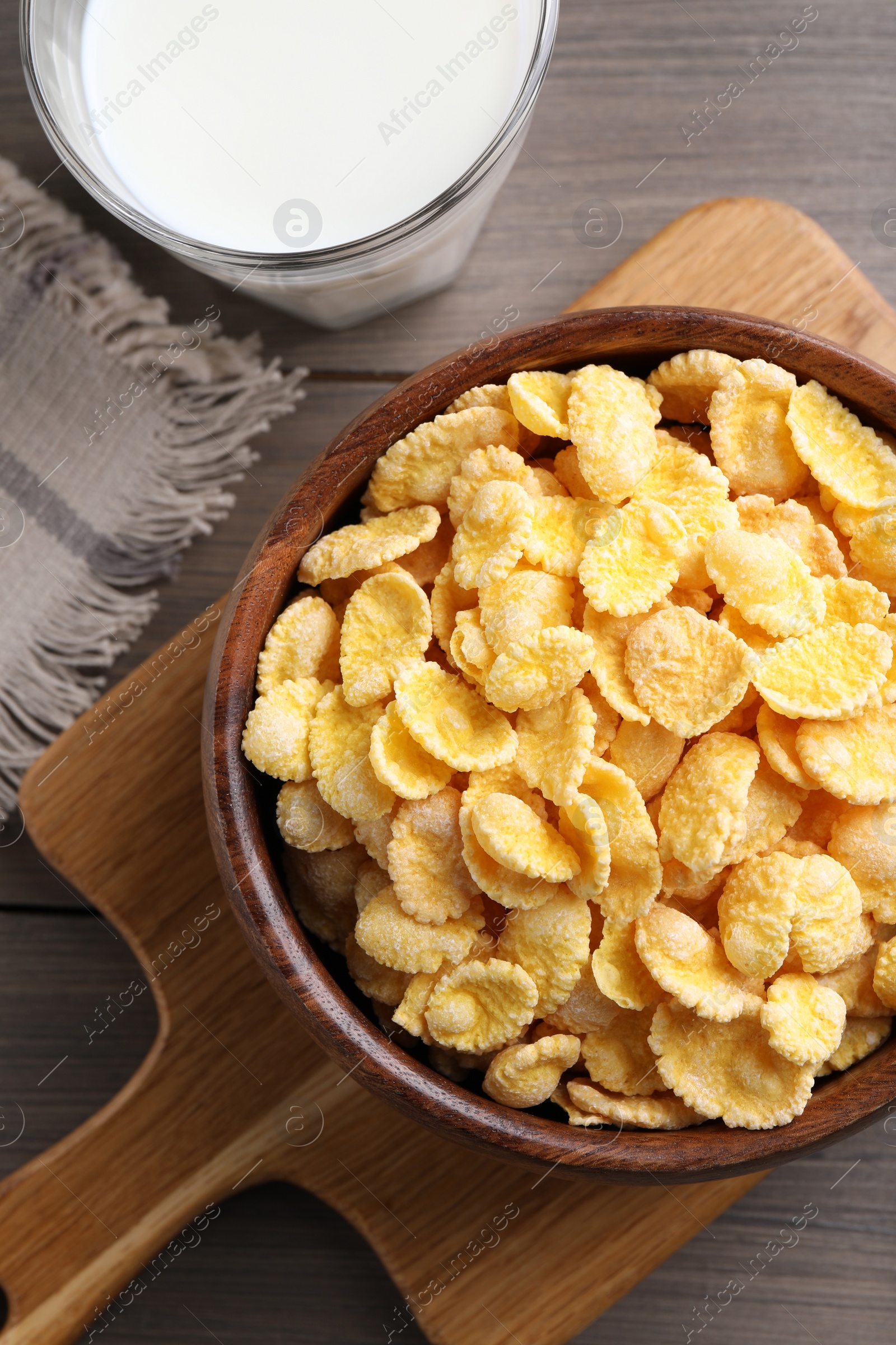 Photo of Tasty crispy corn flakes and glass of milk on wooden table, flat lay