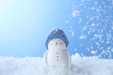 Photo of Cute decorative snowman on artificial snow against light blue background