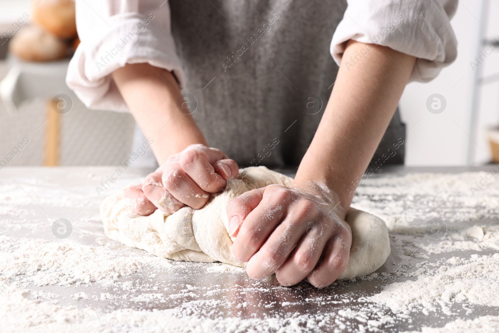 Photo of Woman kneading dough at table in kitchen, closeup