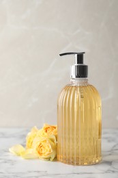 Photo of Stylish dispenser with liquid soap and beautiful flowers on white marble table