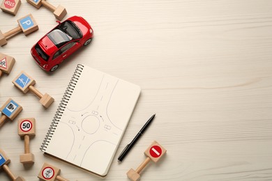 Many different miniature road signs, notebook and toy car on white wooden background, flat lay with space for text. Driving school