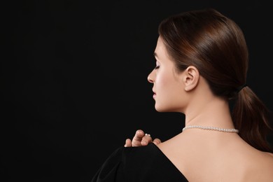 Photo of Young woman wearing elegant pearl jewelry on black background, back view. Space for text