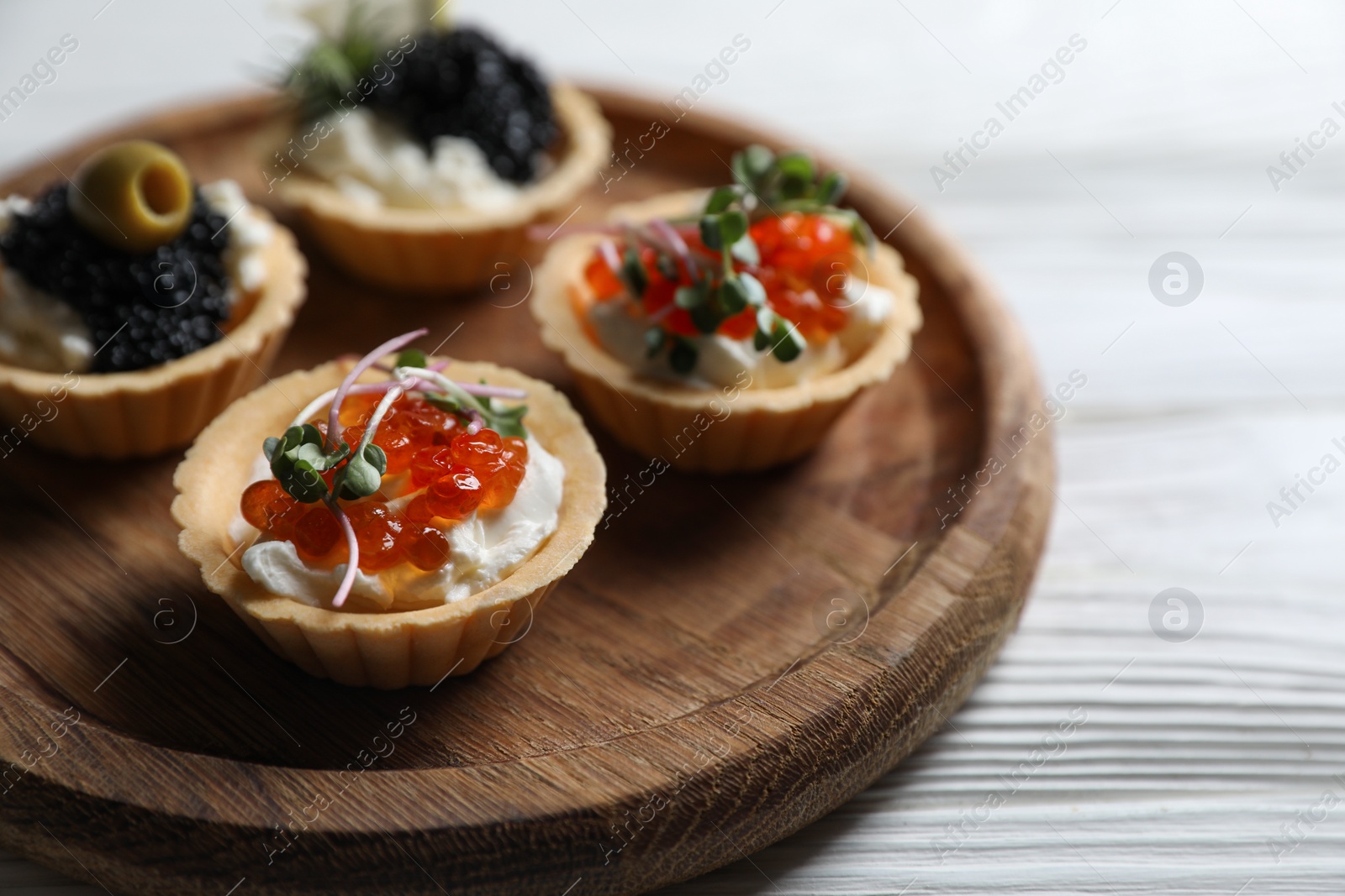 Photo of Delicious tartlets with red and black caviar served on white wooden table, closeup. Space for text