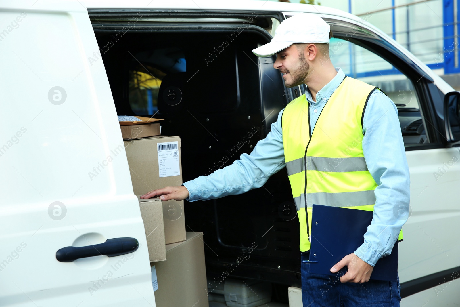 Photo of Young courier holding clipboard near van with parcels outdoors