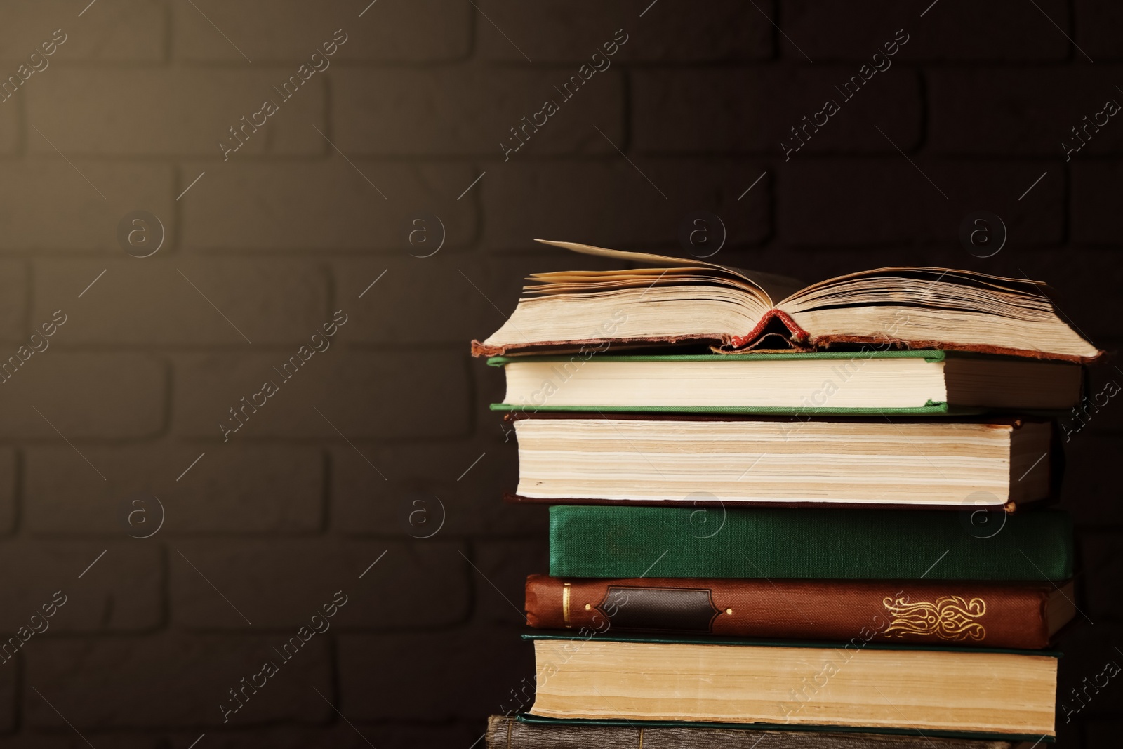 Image of Stack of old hardcover books near brick wall, space for text