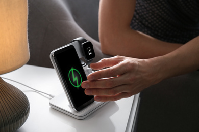 Photo of Man taking smartphone from wireless charger in room, closeup