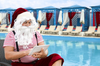 Authentic Santa Claus with tablet working on lounge chair at resort