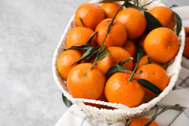 Fresh ripe tangerines and leaves in basket on grey table, closeup