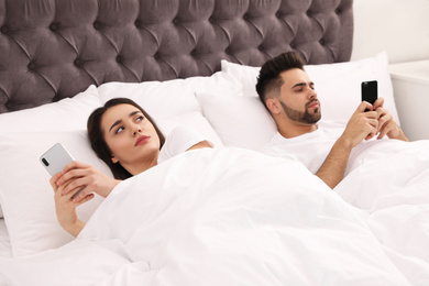 Photo of Young couple with smartphones in bed at home