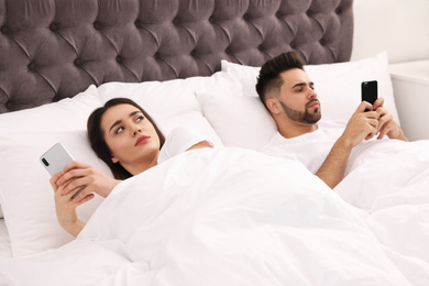 Young couple with smartphones in bed at home