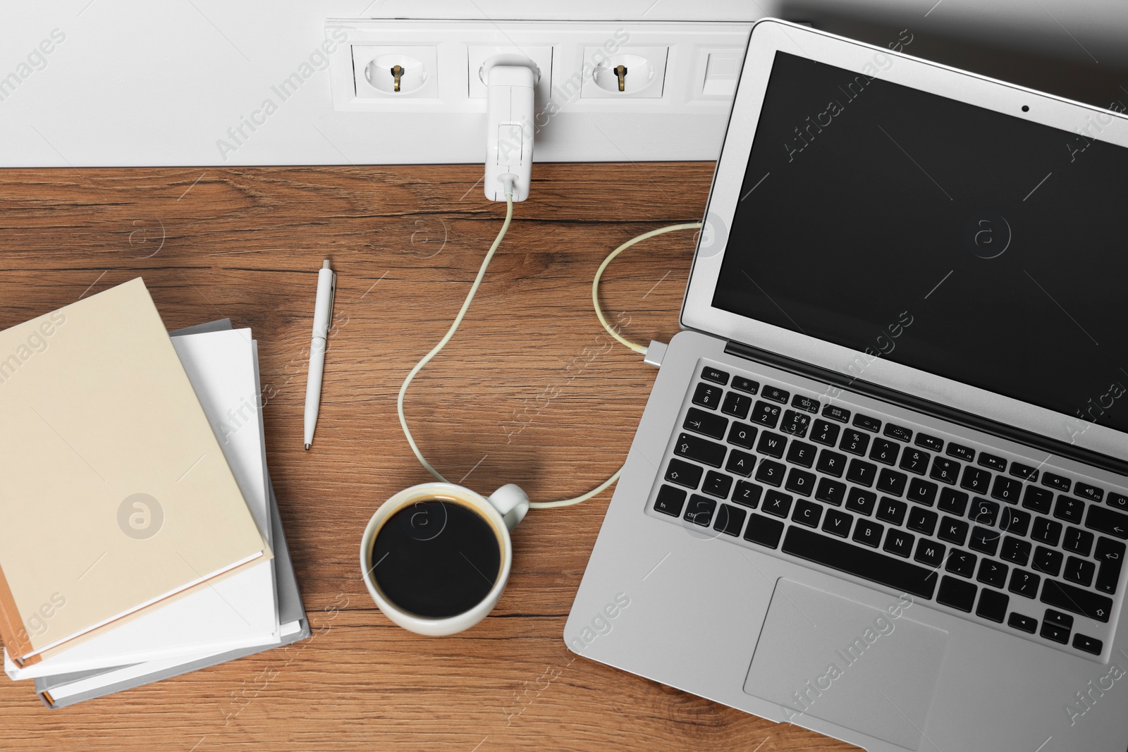 Photo of Modern laptop charging on wooden table, above view