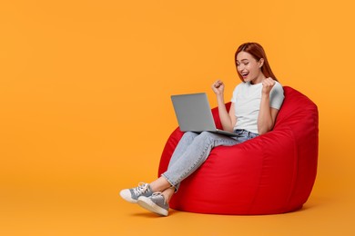Photo of Happy young woman with laptop sitting on beanbag chair against yellow background, space for text