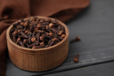 Photo of Aromatic cloves in bowl on grey wooden table, closeup. Space for text