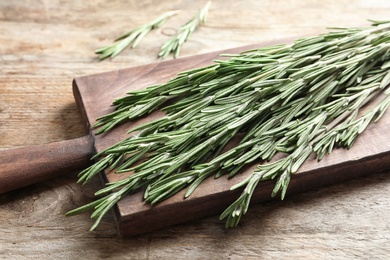 Photo of Board with fresh rosemary twigs on wooden table