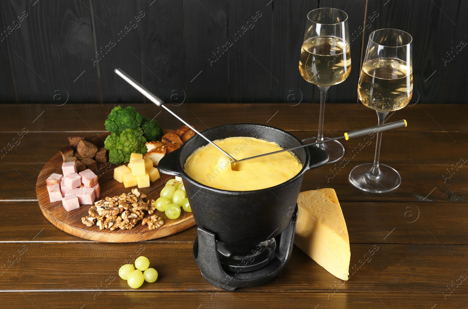 Photo of Fondue pot with melted cheese, glasses of wine and different products on wooden table