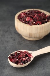 Photo of Hibiscus tea. Wooden bowl with dried roselle calyces and spoon on grey table