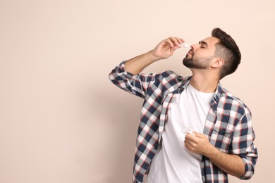 Photo of Man using nasal spray on beige background, space for text
