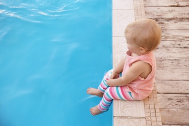 Photo of Little baby sitting near outdoor swimming pool. Dangerous situation