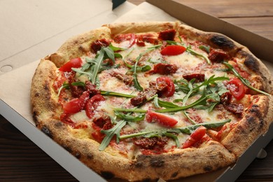 Photo of Tasty pizza with cheese, tomato and arugula in cardboard box on table