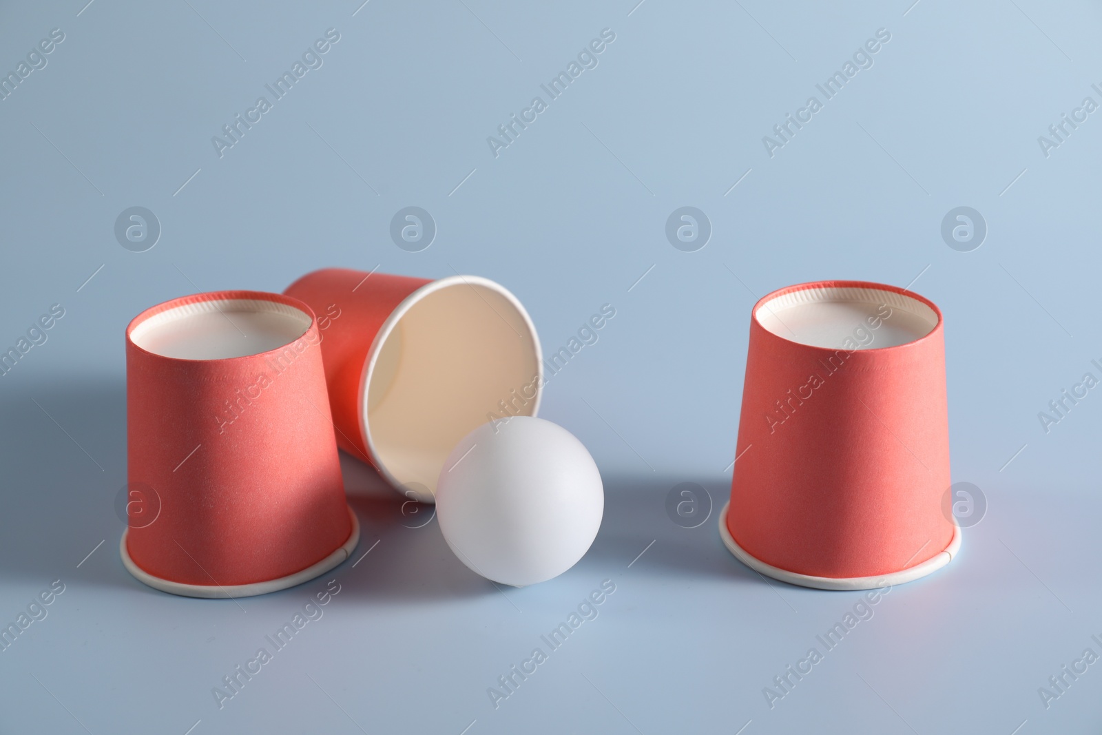 Photo of Shell game. Three red cups and ball on light blue background