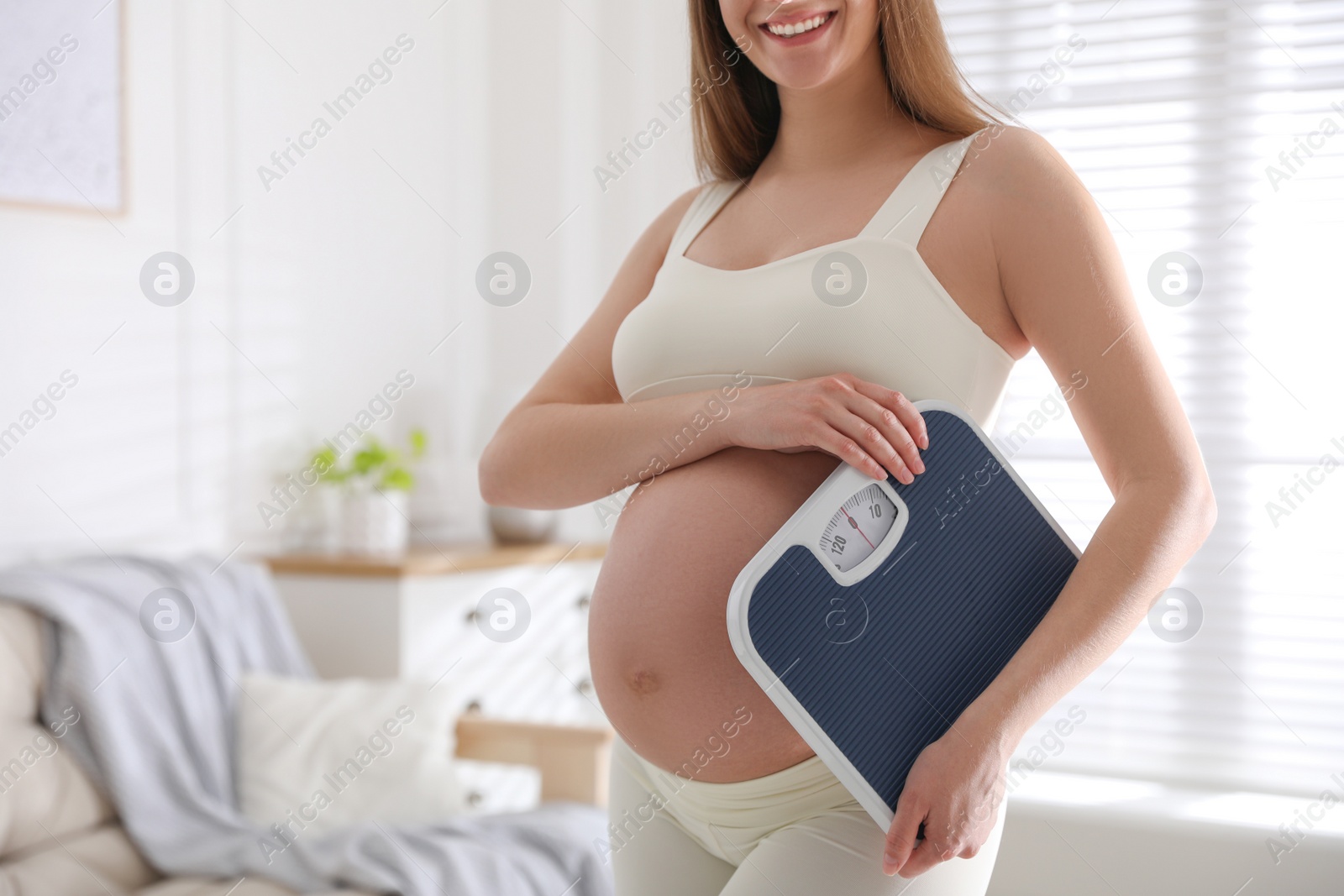 Photo of Young pregnant woman with scales at home, closeup