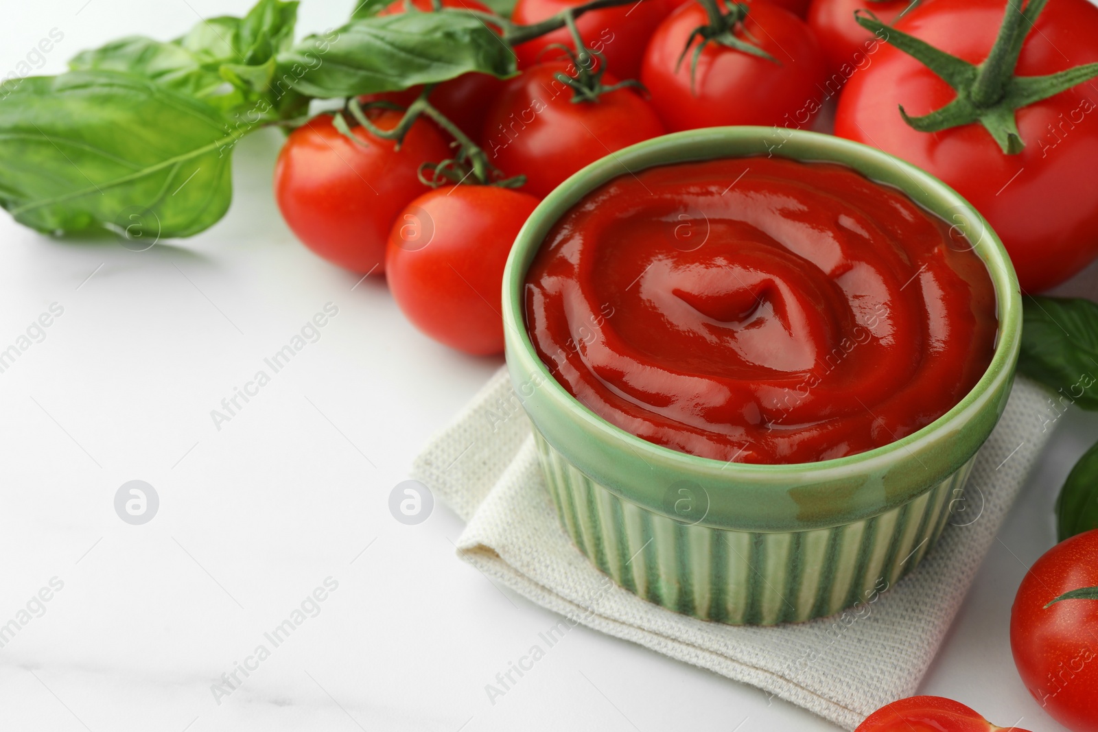 Photo of Bowl of tasty ketchup, tomatoes and basil on white marble table, closeup. Space for text