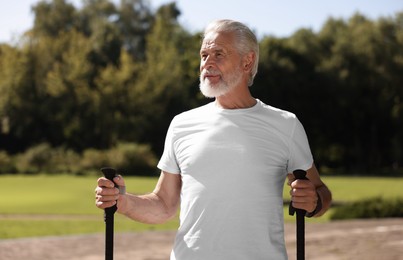 Senior man practicing Nordic walking with poles in park on sunny day