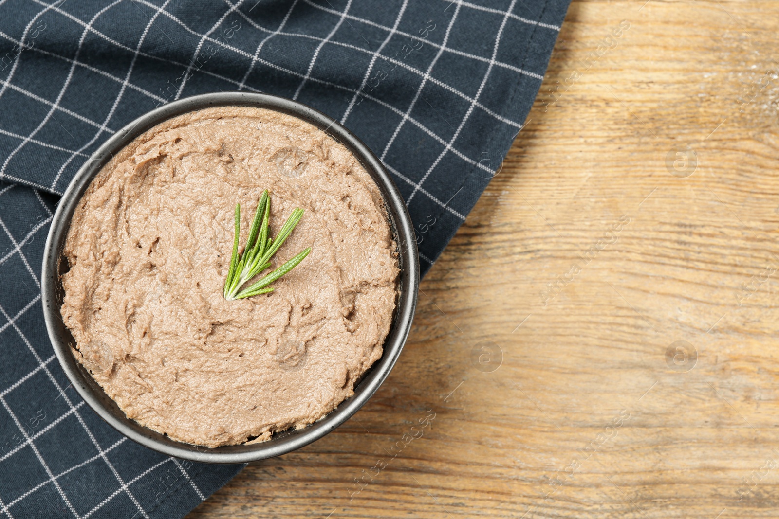 Photo of Tasty liver pate with rosemary in bowl on wooden table, top view. Space for text