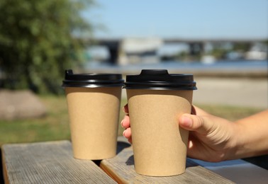 Photo of Woman taking cardboard coffee cup with plastic lid at wooden table outdoors, closeup