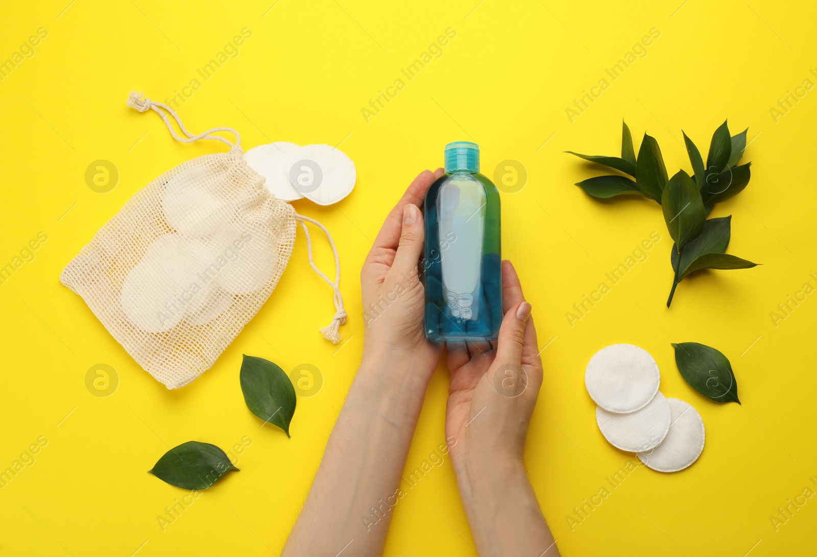 Photo of Woman holding makeup removal product on yellow  background, top view